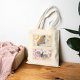 Load image into Gallery viewer, Beige tote bag with butterfly designs on a wooden surface with a white wall and plant in the background