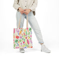 Load image into Gallery viewer, Person holding a colorful tote bag with fruit and vegetable pattern on a white background
