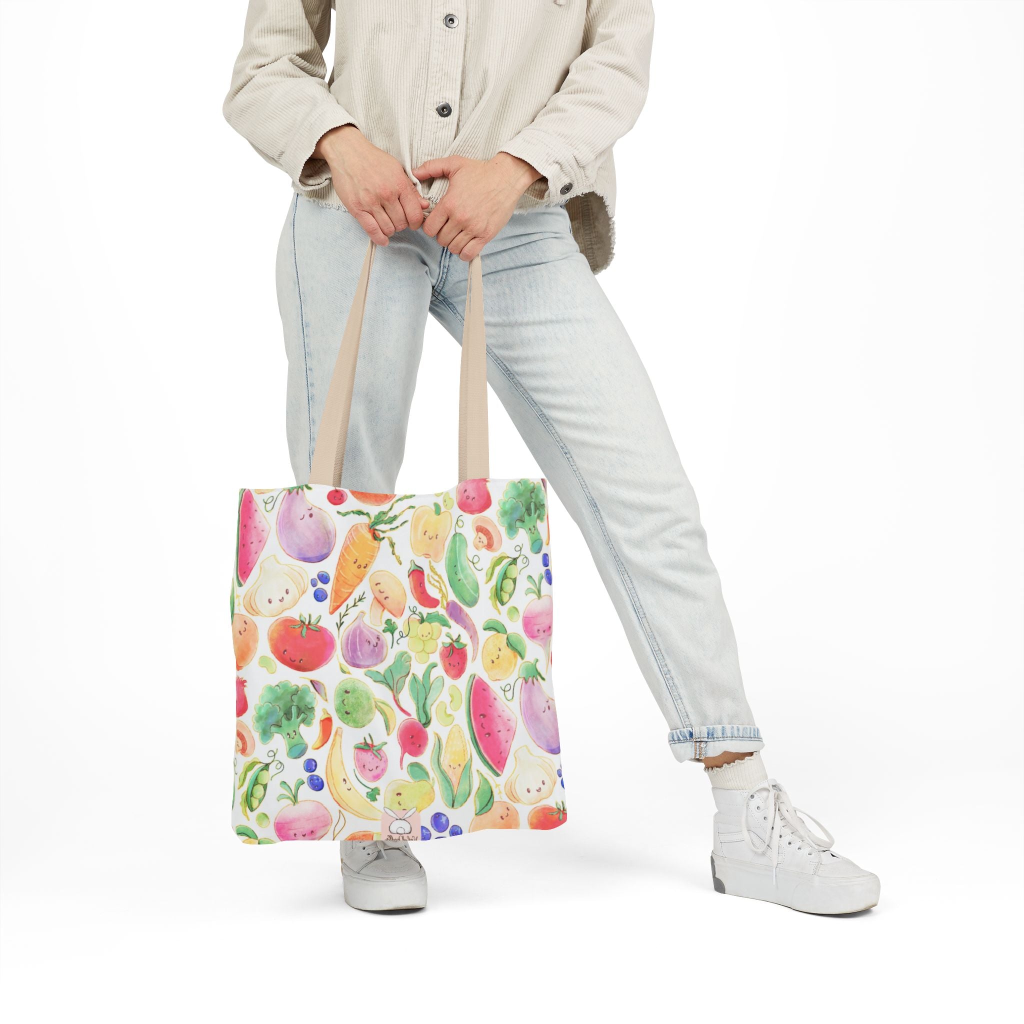 Person holding a colorful tote bag with fruit and vegetable pattern on a white background