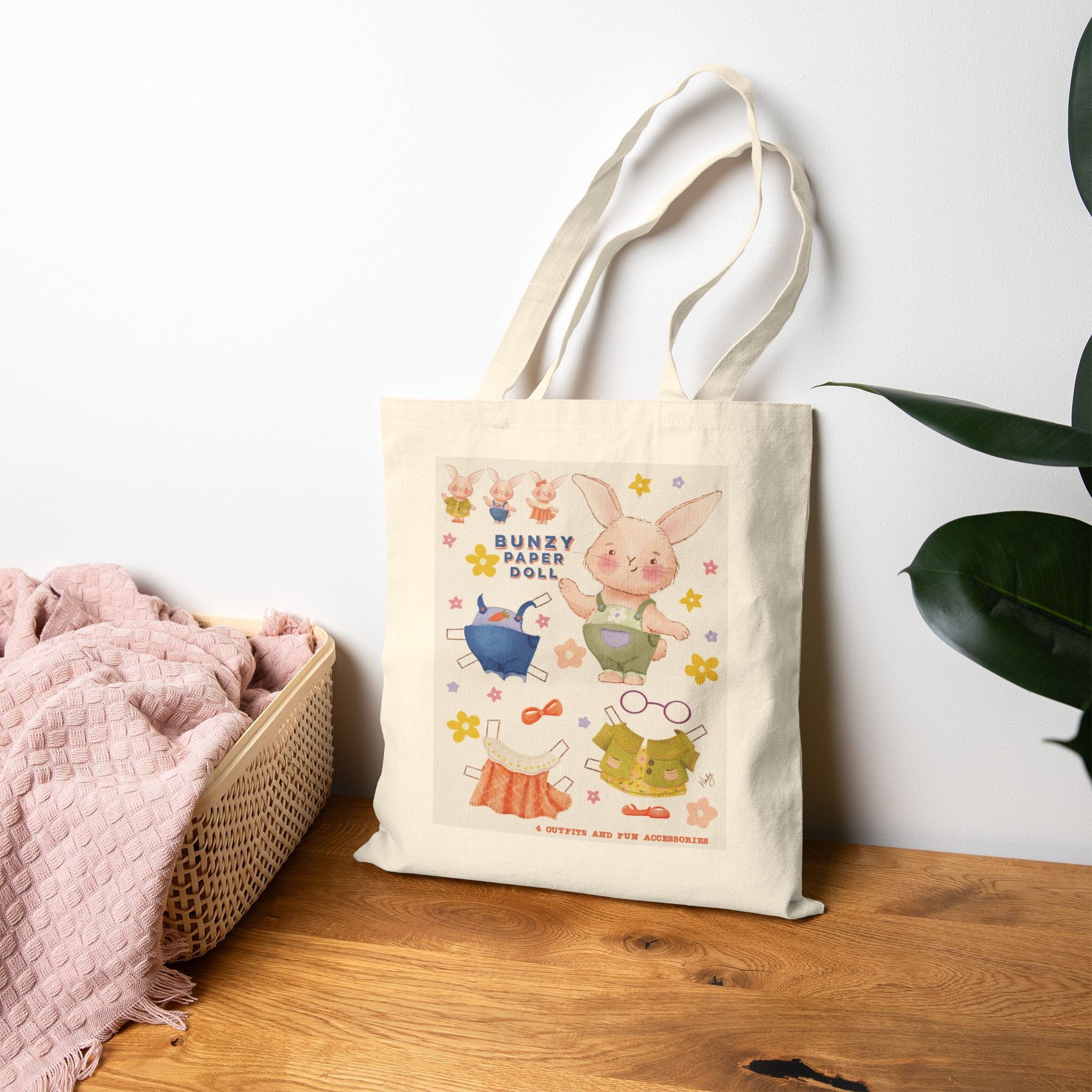 Tote bag with cartoon bunny design on a wooden surface with a white wall and plant in the background