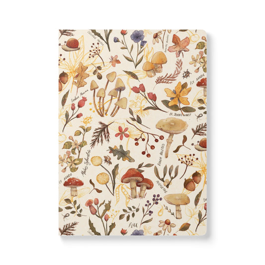 A vertical notebook or journal with a cream-colored cover decorated with a dense, vintage-style botanical  illustration pattern featuring mushrooms, leaves, berries, and small handwritten labels.