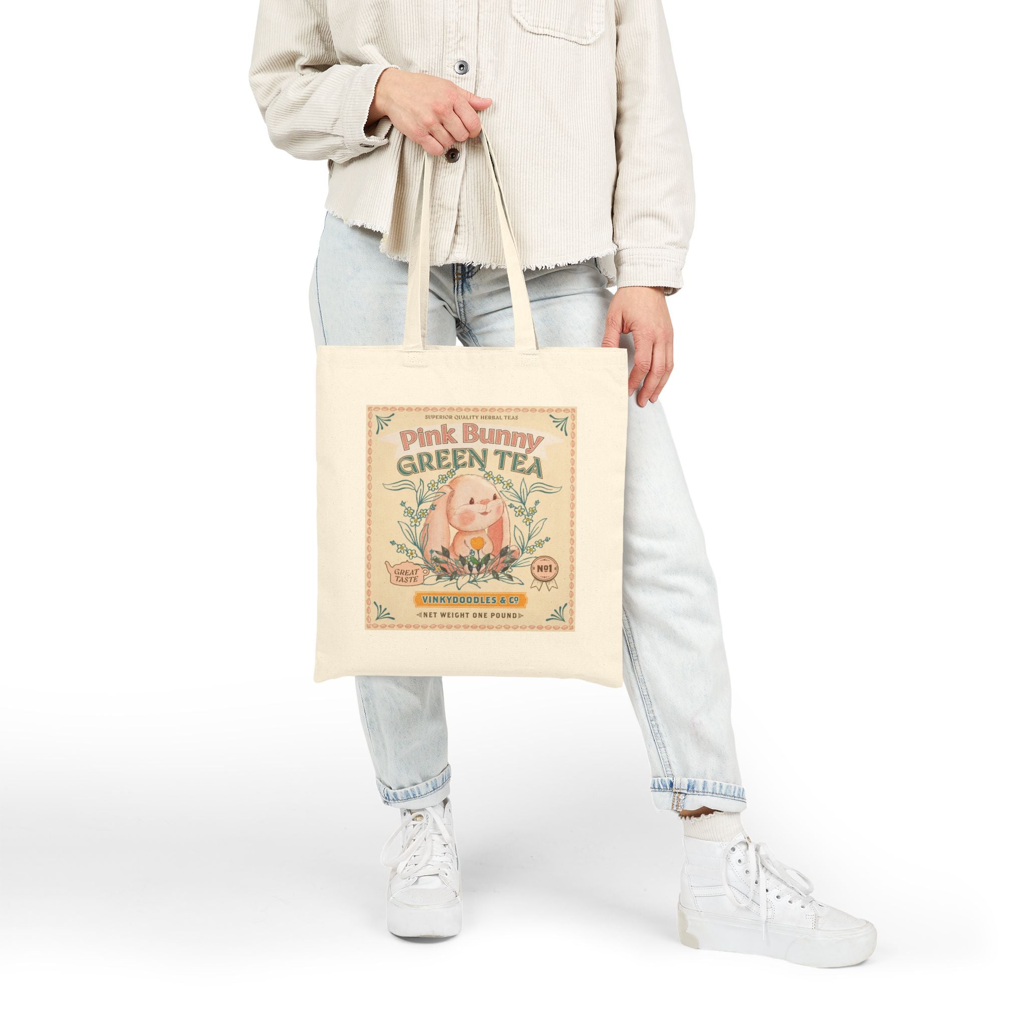 Person holding a tote bag with 'Pink Bunny Green Tea' design on a white background