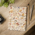 Load image into Gallery viewer, A flat-lay view of a notebook with a vintage-style botanical mushroom pattern on its cover, placed on a rustic wooden desk next to a pencil, a pen, and a camera.
