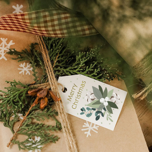 Gift wrapped in brown paper with greenery, a plaid ribbon, and a 'Merry Christmas' tag.