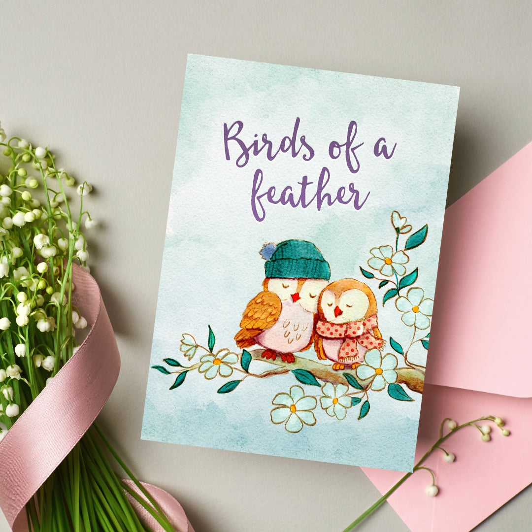 Greeting card with owls and 'Birds of a feather' text, surrounded by flowers and ribbons.