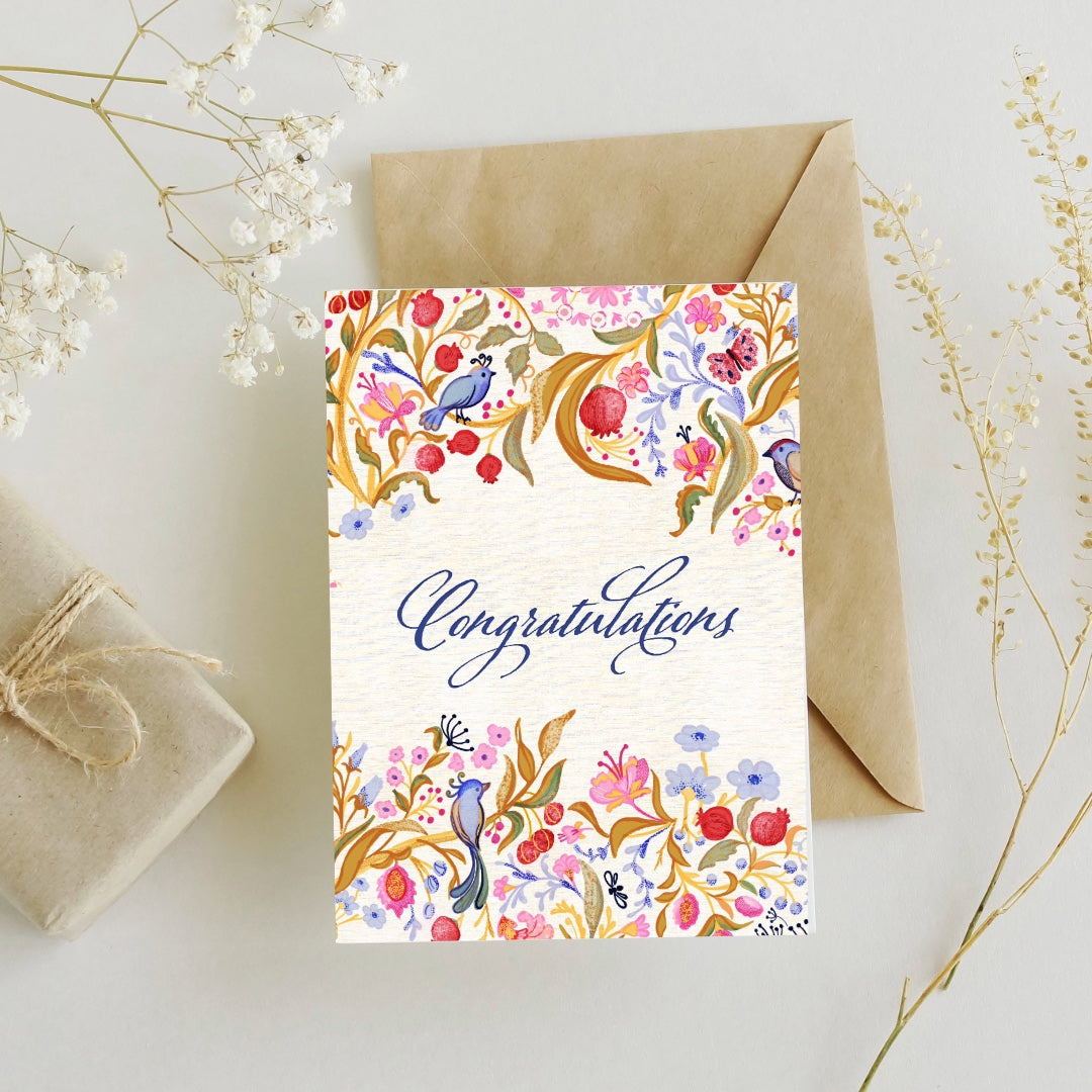 Greeting card with floral design and 'Congratulations' text, accompanied by a brown envelope and gift box on a light background.